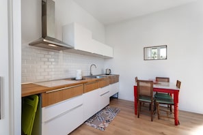 A modern kitchen with white cabinets, a stainless steel range hood, and a dining area with a red table and wooden chairs.