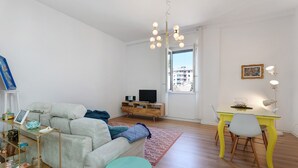 A living room with a sofa, a coffee table, a TV, a dining table with chairs, and a window with a view.