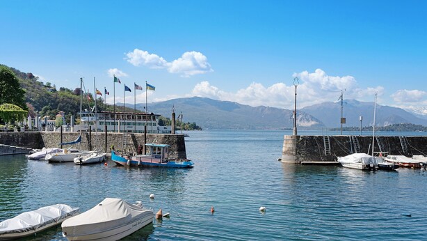 A marina with boats docked, a pier, and mountains in the background.