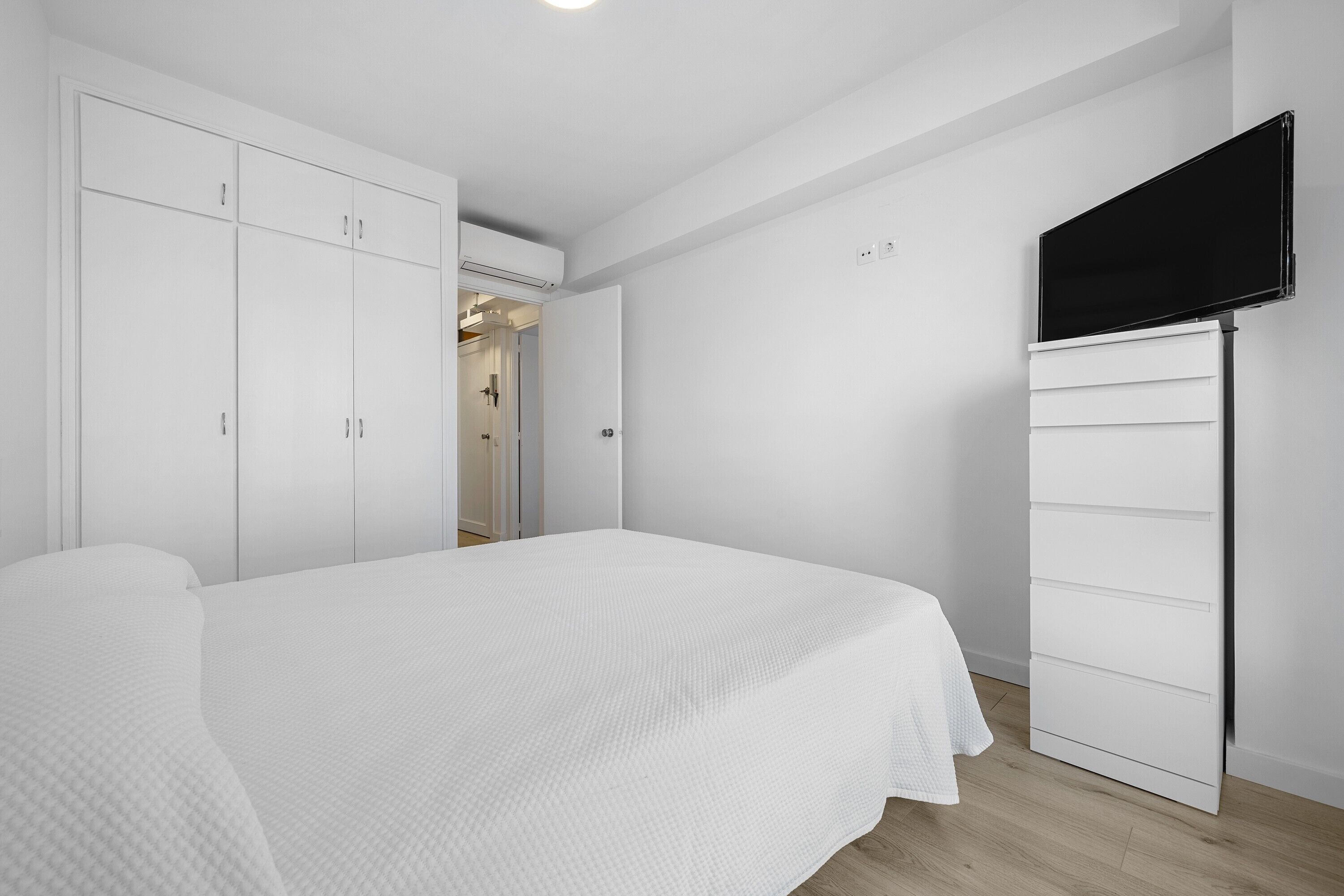 A bedroom with a bed, white wardrobe, and a mounted TV.
