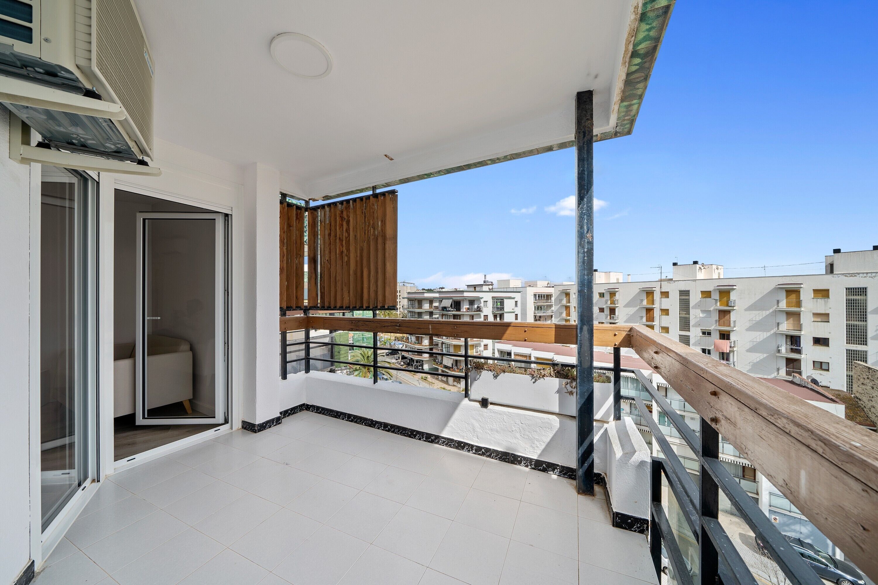 A balcony with a view of surrounding buildings, a sliding glass door, and a wooden railing.
