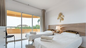 A hotel room with two beds, a balcony, a view of the sea, and a decorative wall piece.