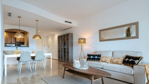 A modern living room with a sofa, coffee table, and dining area with chairs and a kitchen in the background.