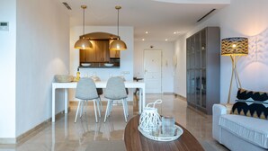 A modern living room with a sofa, a dining table with chairs, a kitchen area with cabinets, and pendant lighting.