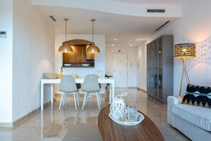 Un salon moderne comprenant un canapé, une table à manger avec des chaises, un coin cuisine avec des placards et un éclairage suspendu.