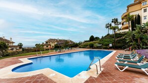 A swimming pool with a tiled deck, lounge chairs, and a view of residential buildings.