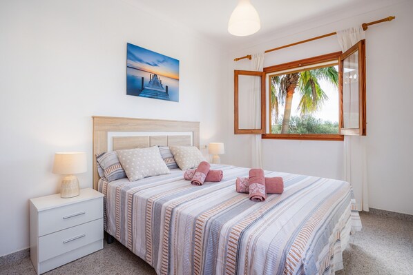 Une chambre à coucher avec un lit, des tables de chevet, une lampe, un tableau et une fenêtre avec des rideaux.