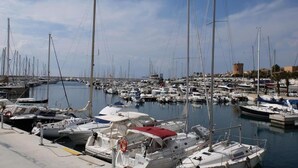 Un port de plaisance où sont amarrés de nombreux bateaux, un ciel dégagé et un bâtiment visible au loin.