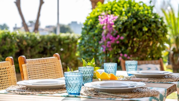 A table set outdoors with wicker chairs, blue glassware, plates, and a woven placemat. - Holiday Home 'Apt Con Piscina Y Jardín' with Shared Pool, Wi-Fi and Air Conditioning (Puerto Pollensa)
