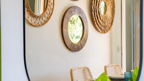 A dining area with wicker chairs, a round table, and three wall-mounted mirrors. - Holiday Home 'Apt Con Piscina Y Jardín' with Shared Pool, Wi-Fi and Air Conditioning (Puerto Pollensa)