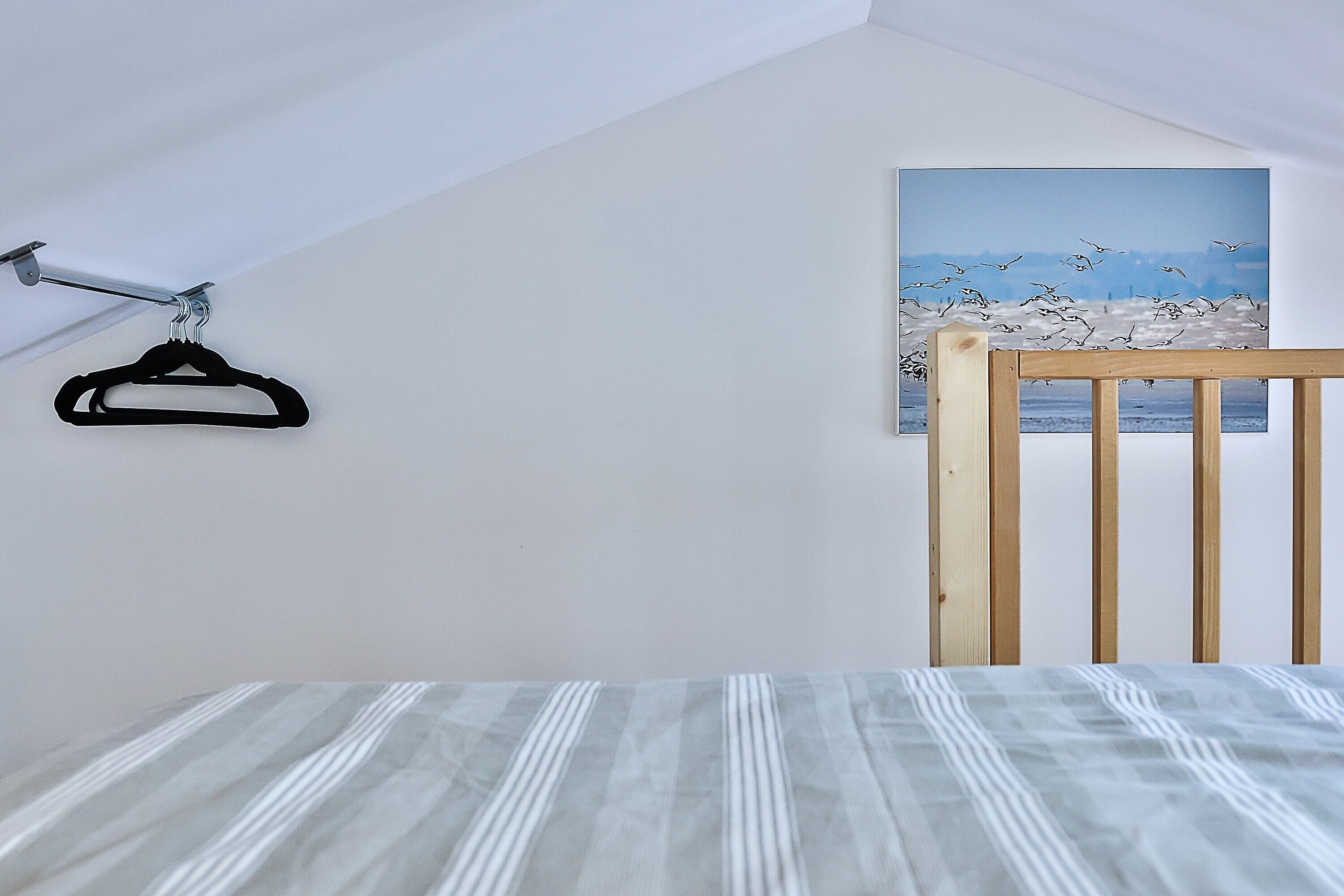 A bedroom with a bed, a wooden chair, a coat rack, and a painting of birds.