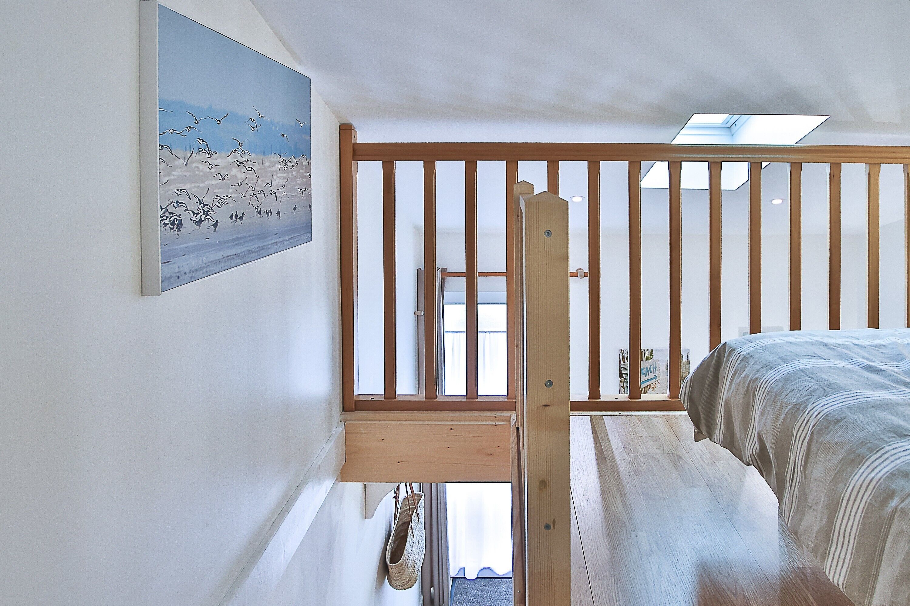 Une chambre à coucher avec un lit en bois, un tableau au mur, un puits de lumière et une vue sur l’extérieur.