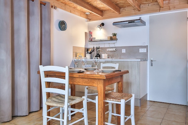 A dining area with a wooden table and white chairs, a kitchen with a white refrigerator, and a clock on the wall.