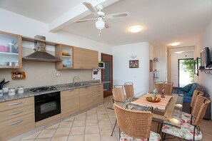 A modern kitchen with a gas stove, oven, and microwave, wooden cabinets, and a dining area with wicker chairs and a glass table.