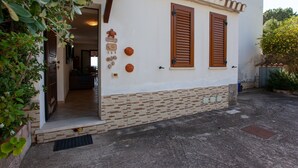 A building with a white facade, wooden shutters, and a stone base. - Vacation Home Casa sulla Spiaggia 1 with Sea-View, Terraces & Garden (Orosei)