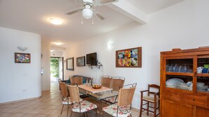 A dining area with a glass-top table, wicker chairs, a wooden cabinet with glass doors, and artwork on the walls. - Vacation Home Casa sulla Spiaggia 1 with Sea-View, Terraces & Garden (Orosei)