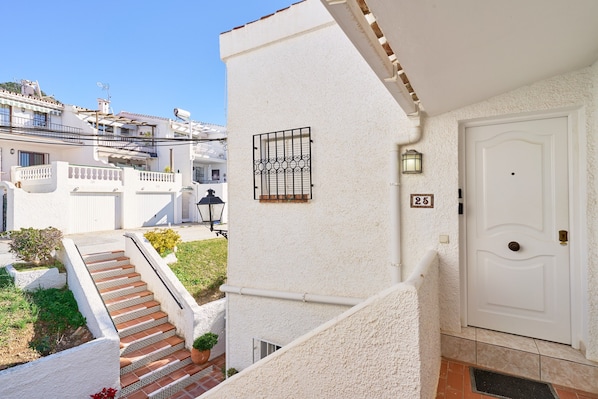 A white building with a door, a window with a metal grill, and a staircase leading to a balcony. - Apartment 'Los Robles ' with Sea View, Wi-Fi and Air Conditioning (Nerja)