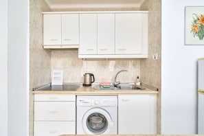 A compact kitchen with white cabinets, a built-in dishwasher, a kettle, and a sink with a faucet. - Apartment 'Los Robles ' with Sea View, Wi-Fi and Air Conditioning (Nerja)