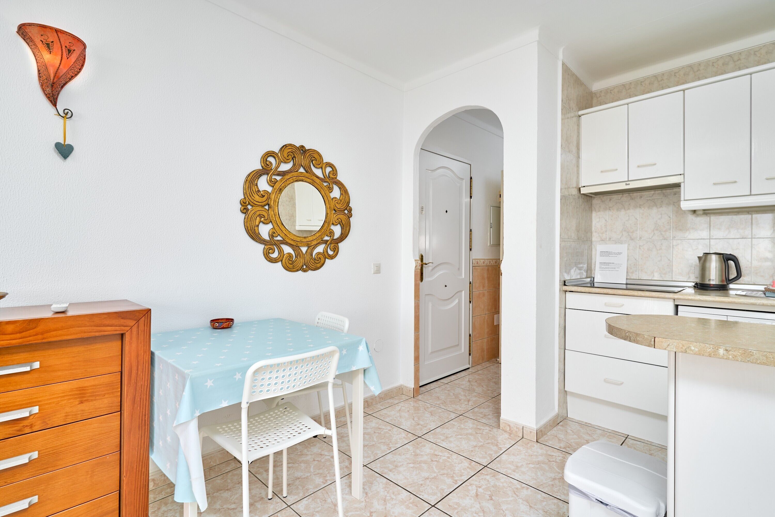 A compact kitchen with white cabinets, a coffee maker, and a table with a star-patterned tablecloth.