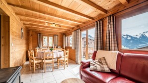 Interior de uma cabana de madeira com área de jantar, um sofá de couro vermelho e vista para as montanhas.