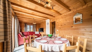 Interior de cabana de madeira com mesa de jantar posta para quatro pessoas, um sofá vermelho e um espelho na parede.