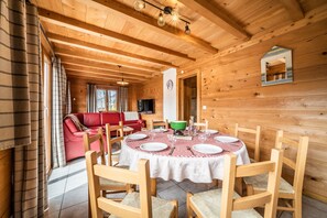 Ein Interieur einer Holzhütte mit einem Esstisch für vier Personen, einem roten Sofa und einem Spiegel an der Wand.
