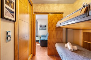 A compact room with a bunk bed, a small seating area with a chair and a table, and a door leading to another room.