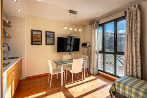 A modern room with a dining table, chairs, a flat-screen TV, a window with curtains, and a bed with a plaid cover.