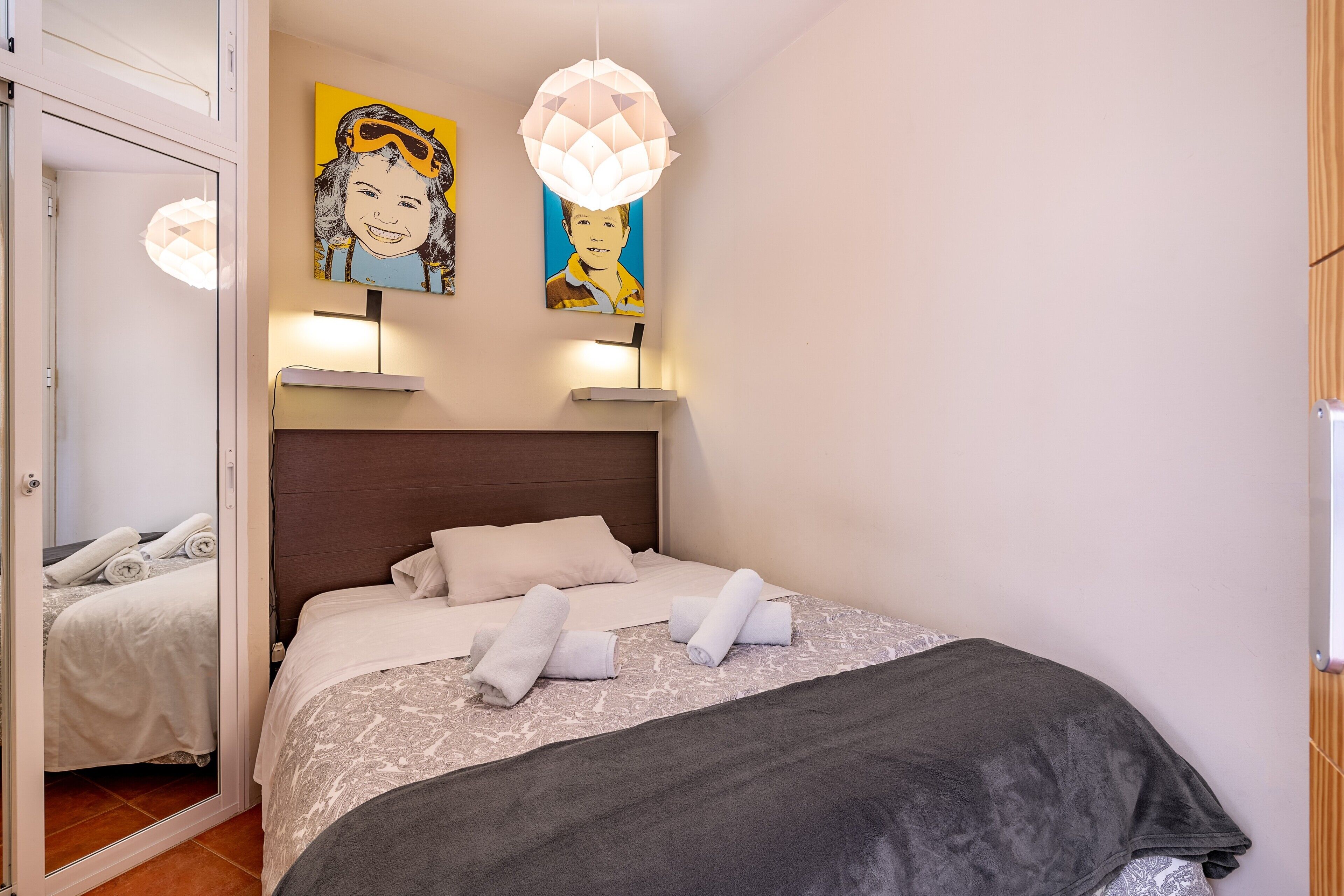 Een net opgemaakt bed met handdoeken, een hoofdbord en wandlampen.