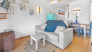 Una sala de estar con un sofá, una mesita, una cesta de mimbre y una pared decorada con marcos.