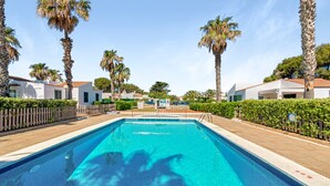 Una piscina con agua cristalina azul, rodeada de palmeras y edificios blancos.