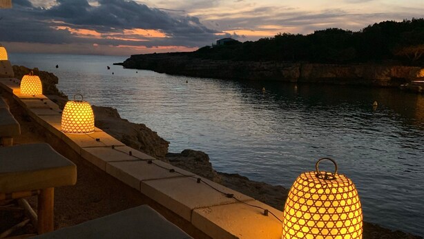Un espacio de descanso junto al agua, con mesas y faroles iluminados.