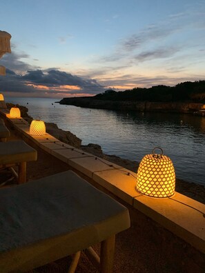 Een terras aan het water met tafels en verlichte lantaarns.