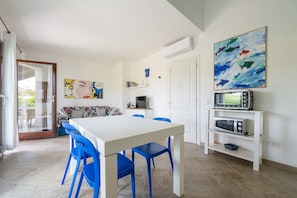 Ein Essbereich mit einem weißen Tisch und blauen Stühlen, eine Küche mit Mikrowelle und Backofen sowie eine Tür zu einem Außenbereich.