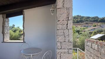 A covered outdoor seating area with a stone wall, a table with chairs, and a view of a landscape with houses and trees.