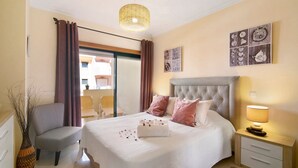 A bedroom with a bed, bedside table, chair, and a view of the outside.