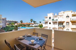 Un balcon avec une table dressée pour le dîner, donnant sur une piscine et des immeubles.