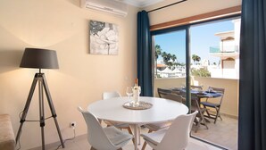 A room with a round table, chairs, a lamp, and a view of a balcony with outdoor furniture.