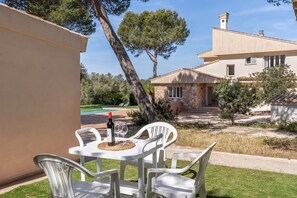 A patio with white plastic chairs and a table, a bottle of wine, and a glass.