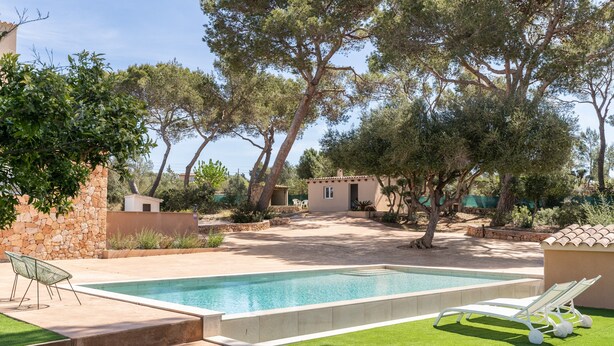 A swimming pool with lounge chairs, a stone wall, and trees.
