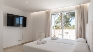 A modern hotel room with a large bed, a flat-screen TV mounted on the wall, and a sliding glass door leading to an outdoor area.