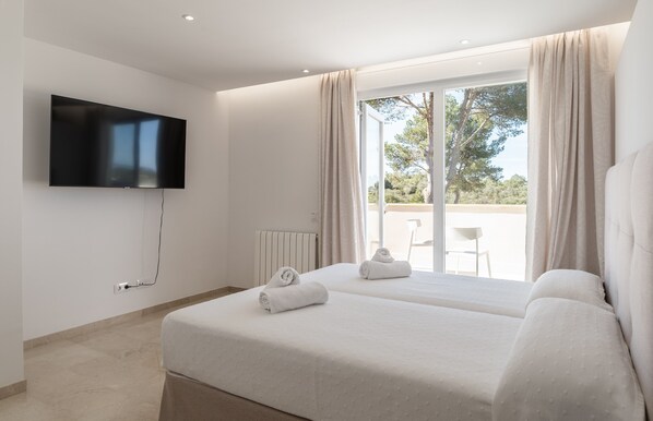 A modern hotel room with a large bed, a flat-screen TV mounted on the wall, and a sliding glass door leading to an outdoor area.
