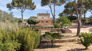 A stone house with a tiled roof, surrounded by trees and dry grass.