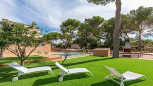 A backyard with a swimming pool, three white lounge chairs, a barbecue grill, and a stone wall.