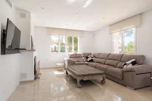 A spacious living room with a large sectional sofa, a wooden coffee table, and a flat-screen TV mounted on the wall.