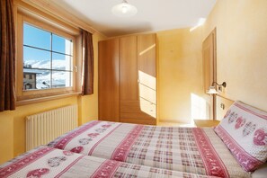 A bedroom with a bed, a window with curtains, a wardrobe, and a bedside lamp. - Apartment 'Al Bait Da Marangona 3' with Mountain View, Shared Garden and Wi-Fi (Livigno)
