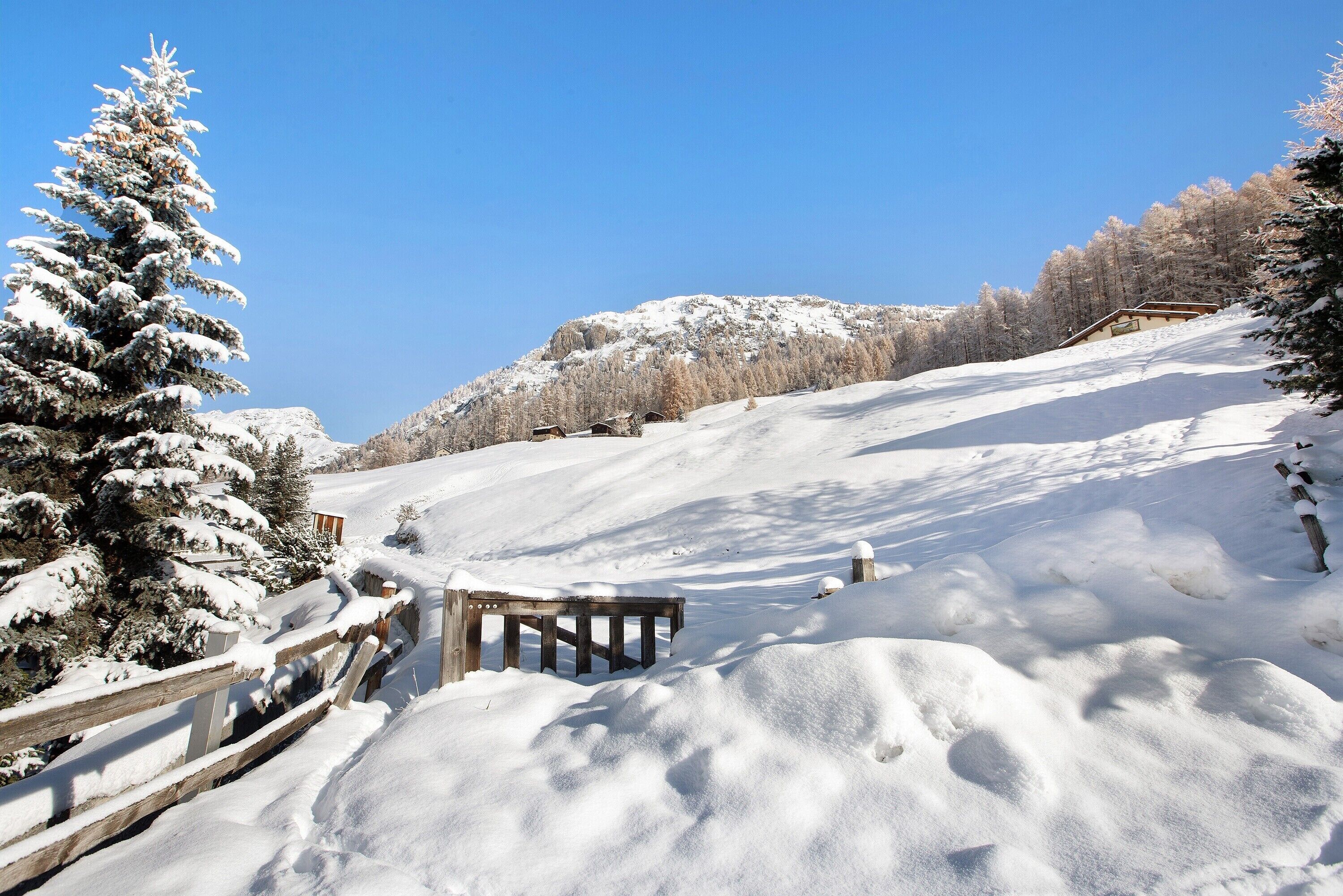 Een besneeerd landschap met een houten hek, een houten constructie en sneeuw bedekte bomen.