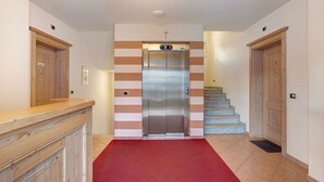 Een hal met een rood tapijt, een houten receptiebalie, een trap en een moderne lift.