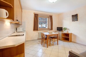 Une cuisine avec une table à manger, des chaises, une fenêtre avec des rideaux, un téléviseur et un radiateur.