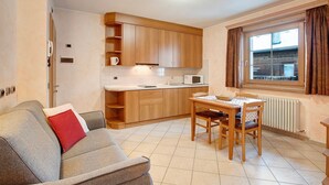 Een gezellige keuken met houten kastjes, een eettafel met stoelen, een bank en een raam met gordijnen.